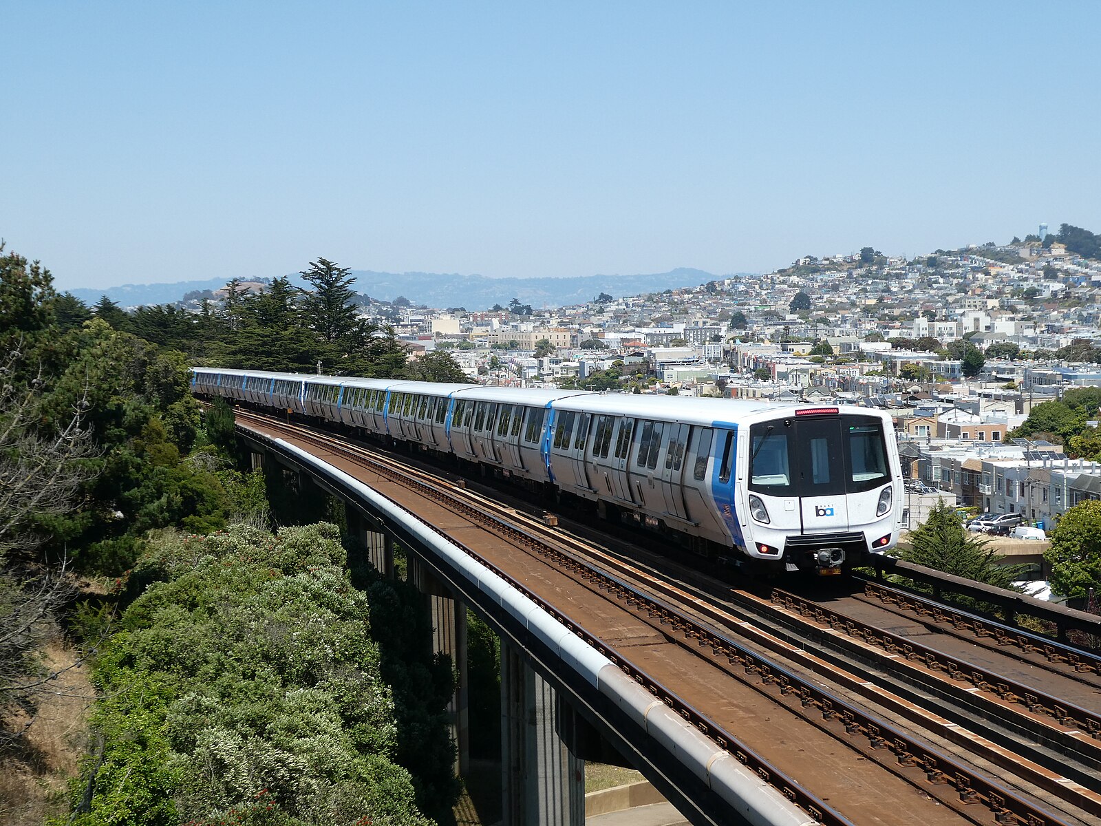 A BART train at surface level with the Bay Area skyline.
